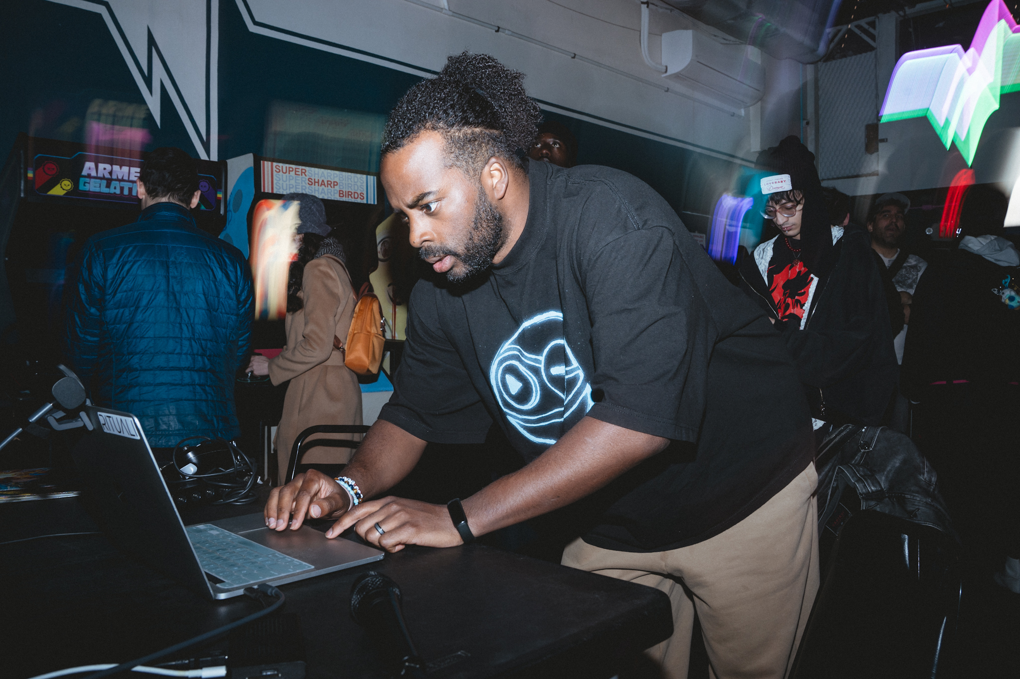Ryan The Son working a laptop between arcade cabinets, A Time to Feel tee